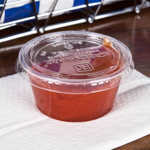 A Fabri-Kal Greenware clear plastic lid on a plastic container of red sauce on a napkin.