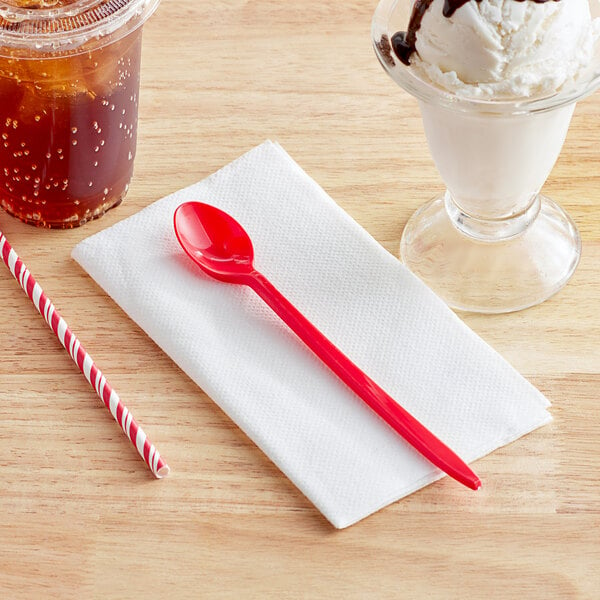 A red Choice plastic spoon on a napkin next to an ice cream sundae and a drink.