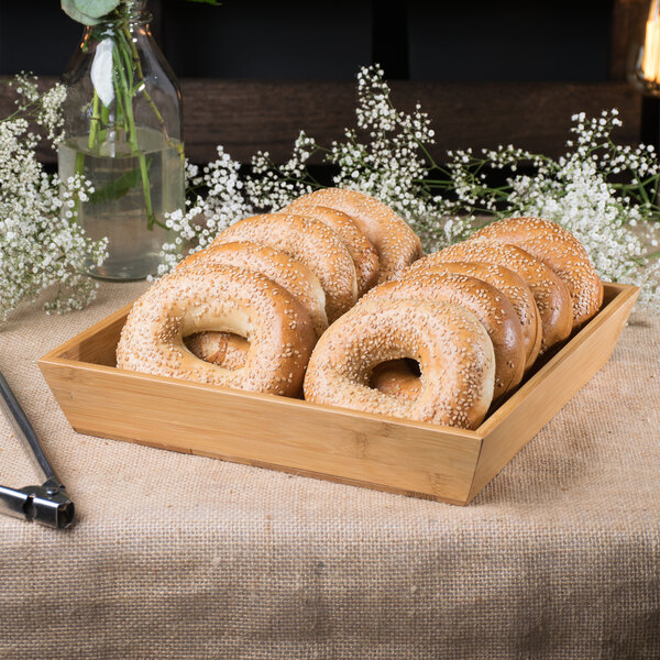 A Clipper Mill bamboo tray holding bagels and flowers on a table in a bakery display.