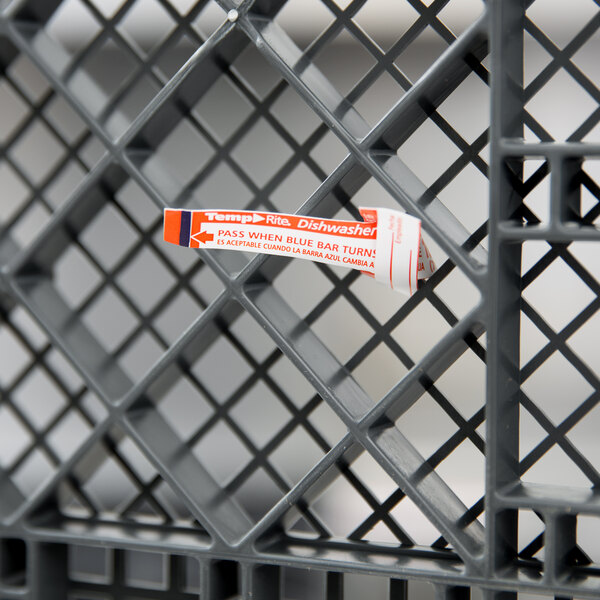 A Taylor TempRite dishwasher test strip package on a metal grid. The package is white and orange with black text.