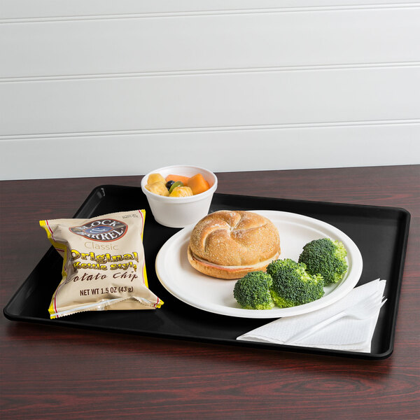 A black Cambro dietary tray with a sandwich, chips, and a drink on it.