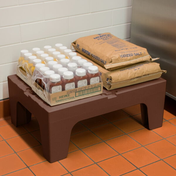 A Cambro brown plastic dunnage rack with brown bags of food and plastic containers on it.