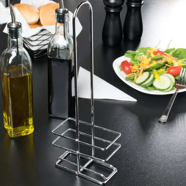 A Tablecraft chrome rack holding a bottle of liquid on a table with a plate of salad.