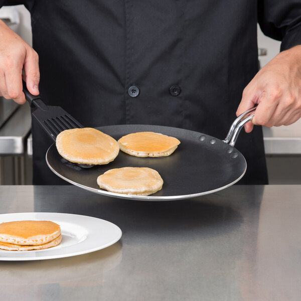 A person cooking pancakes on a Vollrath aluminum non-stick griddle.