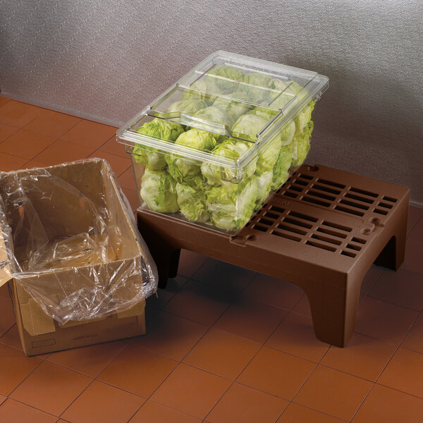 A plastic container with lettuce in it on a brown Cambro dunnage rack step.