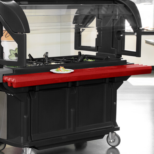 A black and red food cart with a red Cambro tray rail on a counter.