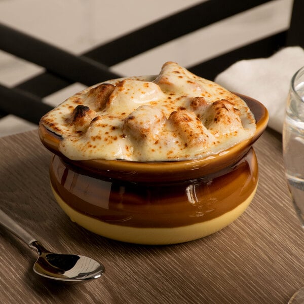A Tuxton onion soup crock filled with French onion soup on a table.