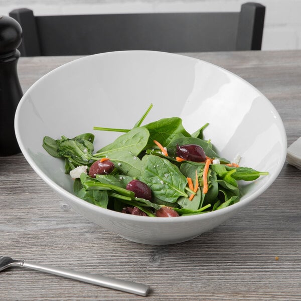 A Tuxton porcelain white china slant bowl filled with spinach salad on a table.