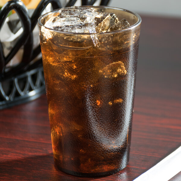 A Cambro amber plastic tumbler filled with ice tea on a table.