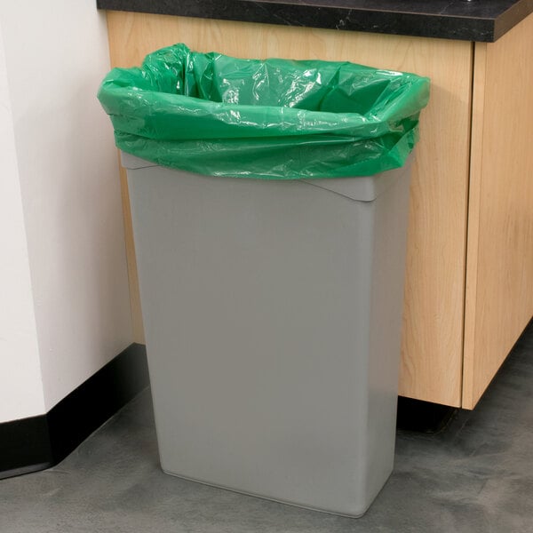 A grey trash can with a green Low Density Eco-Friendly Trash Bag in it.