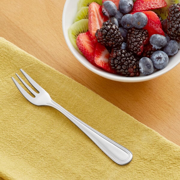 An Acopa Edgewood stainless steel oyster fork on a table with a bowl of fruit.