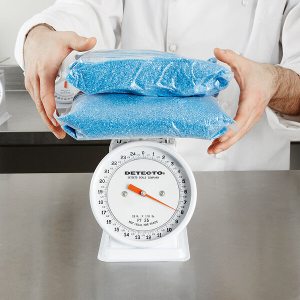 A person weighing blue crystals on a Cardinal Detecto portion scale.