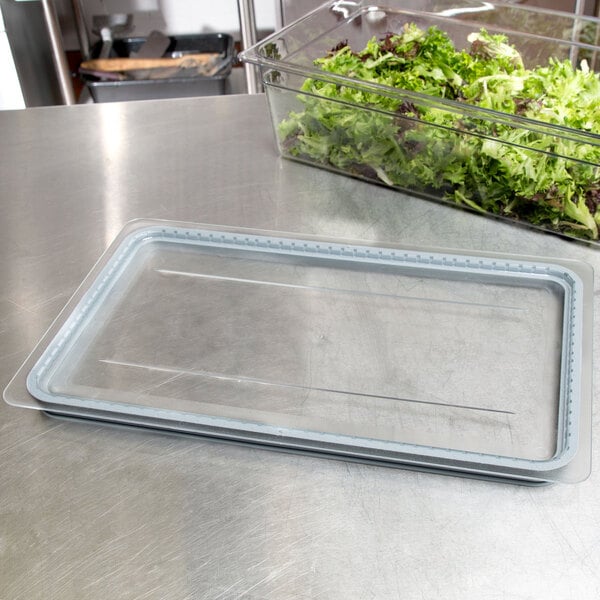 A clear plastic Cambro GripLid covering a container of green lettuce on a clear plastic tray.