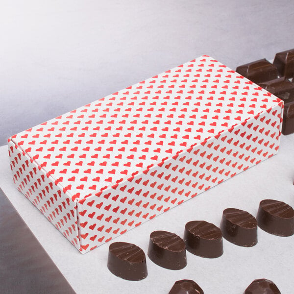 A 1 lb. Valentine's Day heart candy box with red hearts on it next to chocolates.