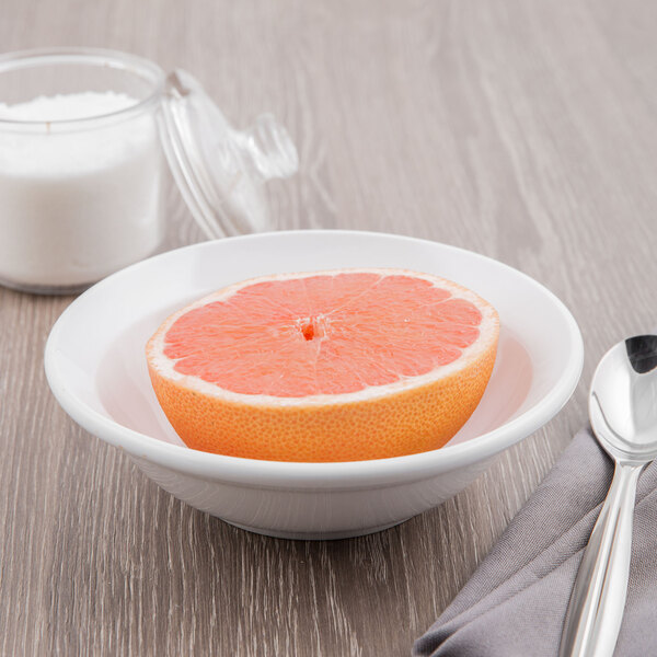 A Libbey Basics white porcelain grapefruit bowl with half a grapefruit and a spoon.