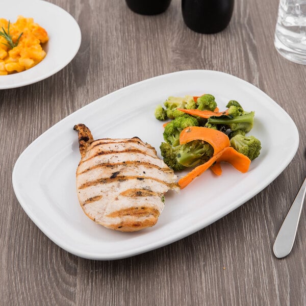 A Libbey bright white porcelain racetrack plate with chicken, broccoli, and carrots on it.