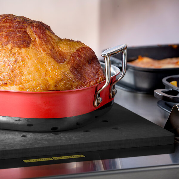 A cooked ham in a pan on a Tablecraft black perforated carving station template.