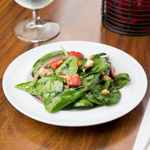 An Arcoroc service plate with a spinach salad topped with red onions.