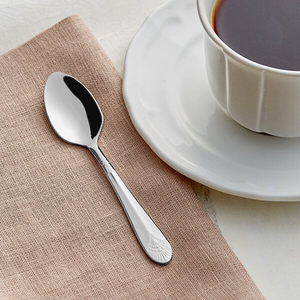 An Acopa Monaca stainless steel demitasse spoon on a napkin next to a cup of coffee.