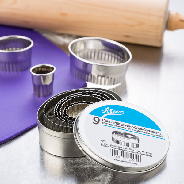 A set of Ateco stainless steel fluted oval cutters and a rolling pin on a metal container.