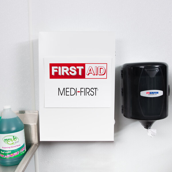 A black Medique first aid kit cabinet with a white label on a shelf.