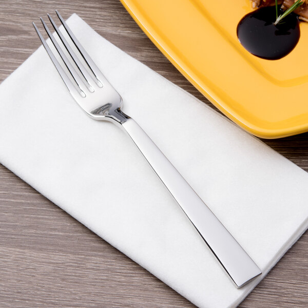 A Bon Chef dinner fork on a napkin next to a plate of food.