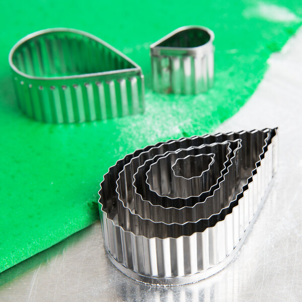 A stainless steel Ateco fluted teardrop cutter set on a green surface.