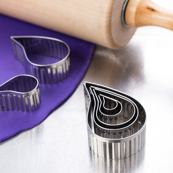 A rolling pin and Ateco stainless steel cookie cutters on a counter.