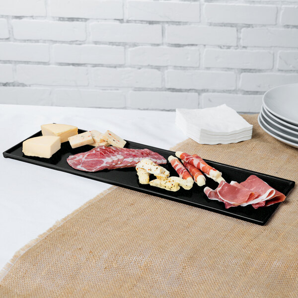 A Tablecraft black cast aluminum long rectangular cooling platter with meat and cheese on a table.