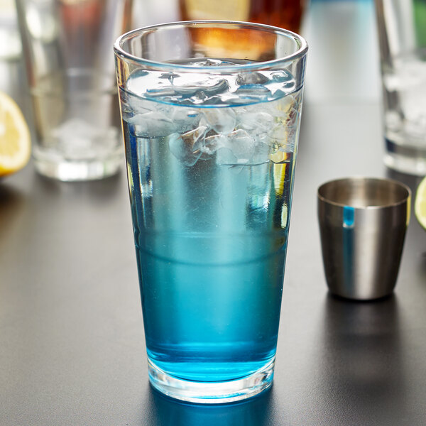 A Libbey stackable mixing glass filled with blue liquid and ice on a table.
