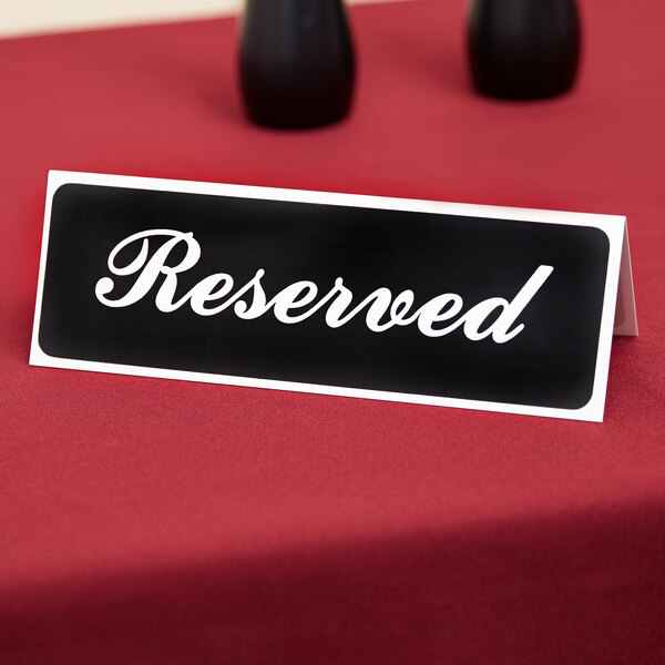 A black Vollrath table tent sign that says "Reserved" on a table in a farm-to-table restaurant.