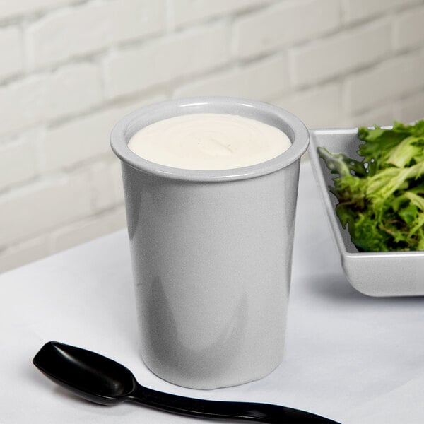 A white bowl of salad in a Tablecraft natural aluminum salad dressing crock with a spoon.