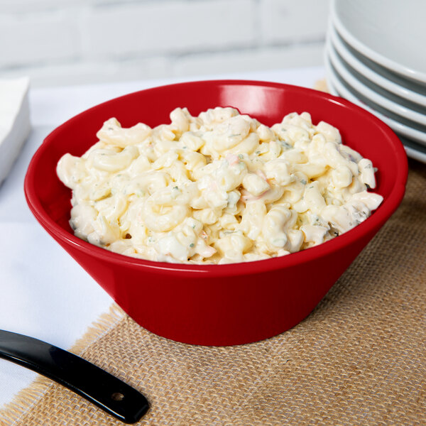 A red Tablecraft round cast aluminum bowl filled with macaroni salad.