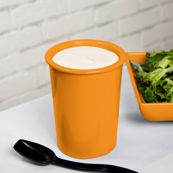 An orange Tablecraft salad dressing crock filled with white liquid on a bowl of lettuce.