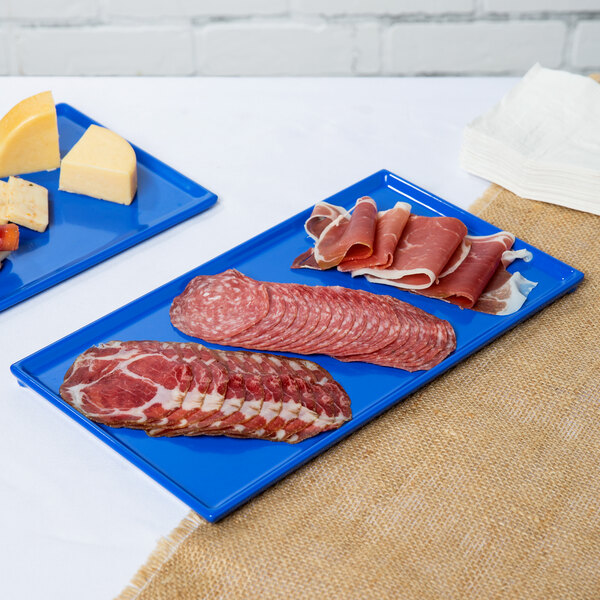 Two Cobalt blue Tablecraft rectangular cast aluminum cooling platters with meat and cheese on them.