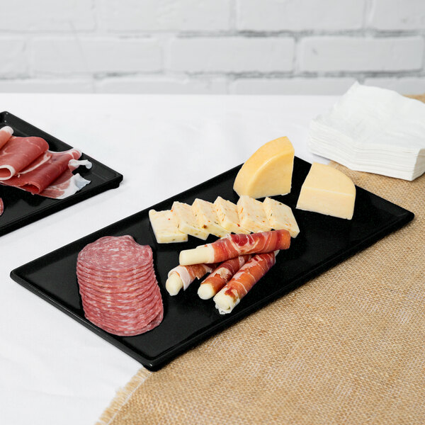 Two black Tablecraft rectangular cooling platters with green speckles holding meat and cheese on a black surface.