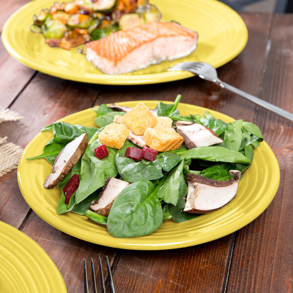 A Fiesta luncheon plate with salad and fish on it on a table.