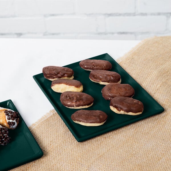 A Tablecraft rectangular hunter green cast aluminum cooling platter holding chocolate covered pastries on a table in a bakery.