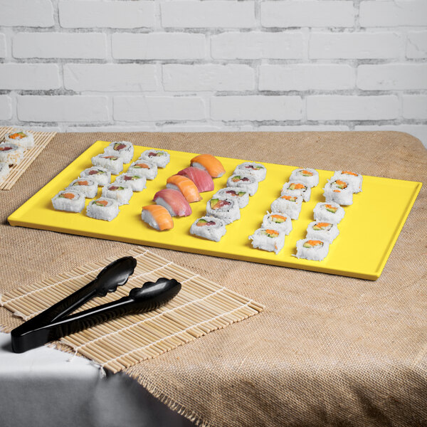 A yellow Tablecraft rectangular cast aluminum cooling platter with sushi on a table.