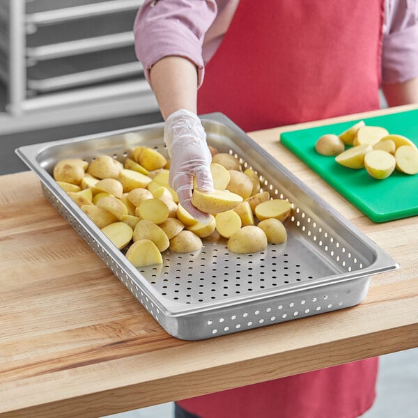 A woman peeling potatoes in a Choice stainless steel steam table pan.
