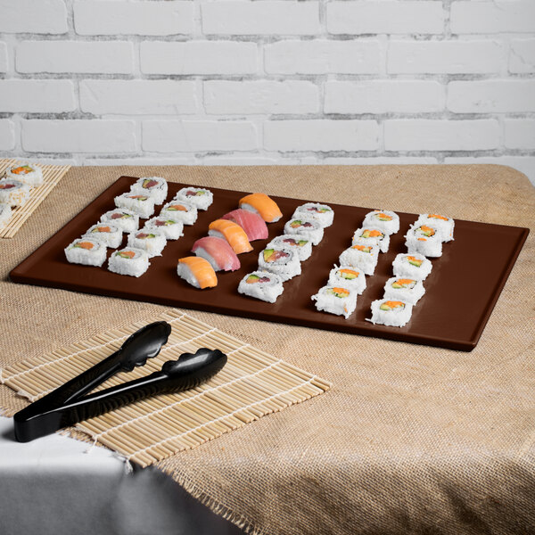 A Tablecraft brown cast aluminum rectangular cooling platter on a table with sushi and tongs.