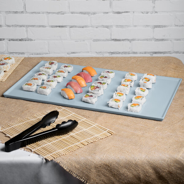 A Tablecraft gray cast aluminum rectangular cooling platter on a table with sushi and tongs.
