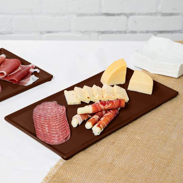 A brown cast aluminum rectangular Tablecraft cooling platter with meat and cheese on it.