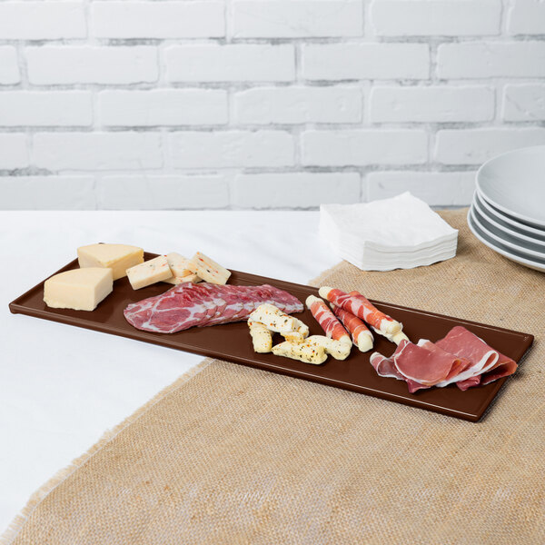 A brown Tablecraft cast aluminum rectangular cooling platter with meat and cheese on it.