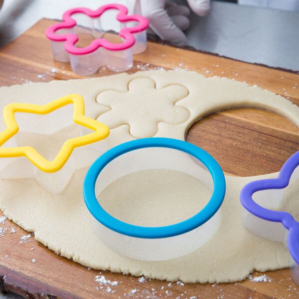 A Wilton plastic cookie cutter set cutting dough on a wooden surface.