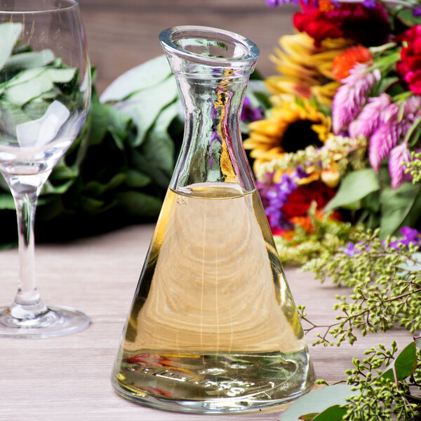 A Stolzle Pisa glass carafe filled with a clear liquid on a table next to a glass of wine.