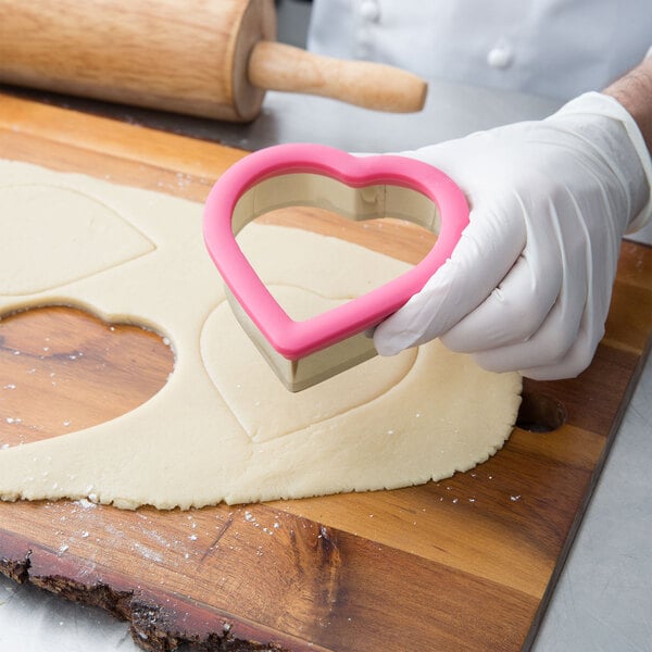 A person in gloves using a Wilton metal heart cookie cutter.