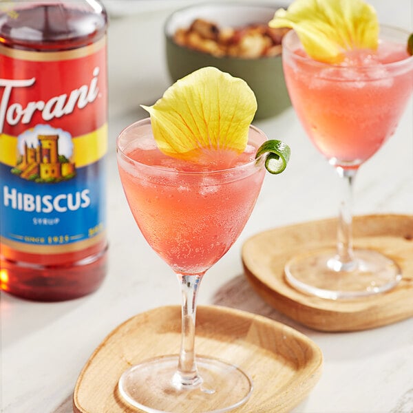 Two glasses of pink Torani Hibiscus drinks with flowers on top.