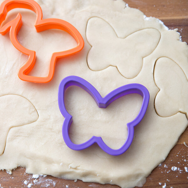 A purple butterfly-shaped Wilton cookie cutter on a piece of dough.