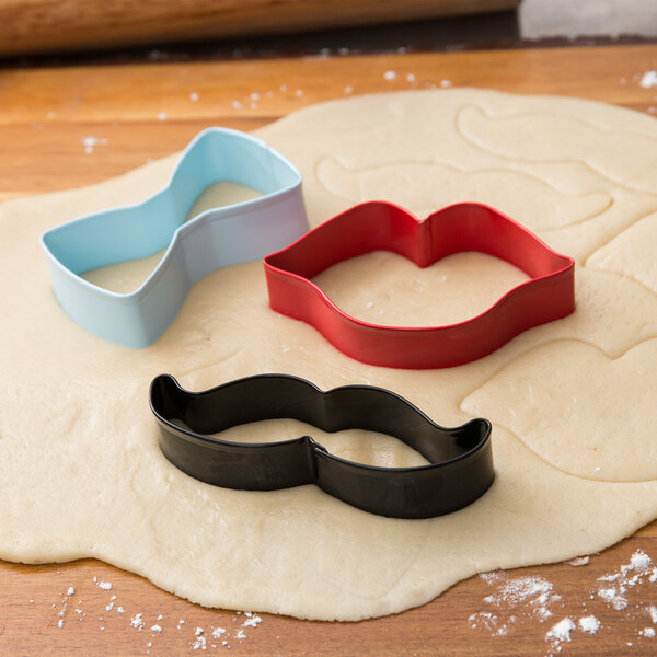 Cookie dough with Wilton metal bow tie, mustache, and lips cookie cutters on top.